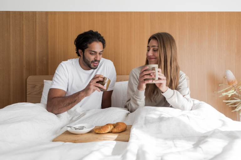 couple drinking coffee and eating croissants on eva bed