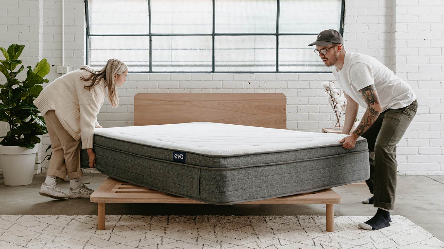 Man and woman putting mattress on bed base 